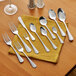 A set of stainless steel flatware including various spoons, forks, and a knife displayed on a yellow napkin.