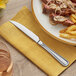 A stainless steel heavy weight steak knife with a serrated edge placed on a yellow napkin.