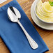 A stainless steel dinner or dessert spoon with a simple decorative handle, placed on a blue napkin.