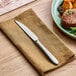 A stainless steel steak knife with a serrated edge placed on a folded brown napkin.