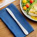 A stainless steel dinner knife placed on a blue napkin next to a plate of food.