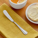 A stainless steel butter spreader with a simple, elegant handle design placed on a yellow napkin.