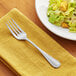 A stainless steel salad fork placed on a yellow napkin next to a plate of salad.