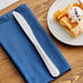 A stainless steel dessert knife placed on a blue napkin next to a plate of dessert.