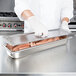 A person wearing gloves uses a Vollrath stainless steel cover to prepare sausages in a steam table pan.