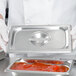 A chef holding a Vollrath stainless steel steam table pan cover filled with sauce.
