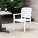 A white Grosfillex Acadia stacking chair on a concrete patio next to a table with drinks.