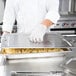 A person using a Vollrath stainless steel cover on a large pan of food.