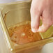 A hand putting a Vollrath amber drain tray into a square plastic container.