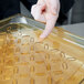 A finger touching a Vollrath amber plastic drain tray.