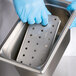 A person in blue gloves using a Vollrath stainless steel drain tray.