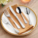 A five-piece set of stainless steel flatware including two forks, a knife, and two spoons, displayed on a plate with a brown napkin.