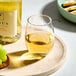 A clear 15 oz. stemless wine glass filled with white wine, placed on a round tray.