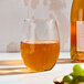 A clear, stemless wine glass filled with a golden liquid, shown on a light surface.