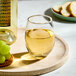 A clear Acopa 12 oz. stemless wine glass filled with white wine, placed on a round tray.