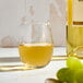 A clear, stemless wine glass filled with white wine, shown next to a wine bottle and green grapes.