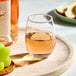 A clear, stemless wine tasting glass filled with rosé wine, placed on a round tray.