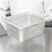 A person in white gloves holding a Vollrath stainless steel pan with holes.