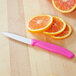 A Victorinox paring knife with a pink handle next to orange slices on a cutting board.