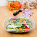 A Sabert clear plastic square bowl filled with salad on a table.