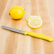 A Victorinox utility knife with a yellow handle slicing a lemon on a table.