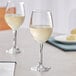 Two Acopa customizable wine glasses filled with white wine on a table.