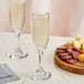 Two Acopa flute glasses of champagne next to cheese on a table.