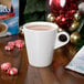 A white mug of Swiss Miss hot chocolate on a table with a peppermint candy on the saucer.