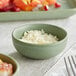 A small sage green bowl filled with white flakes, placed on a light-colored tablecloth.