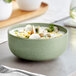 A sage green matte finish bowl filled with a creamy soup garnished with herbs and sliced vegetables.