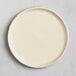 A round, matte, off-white plate with a slightly raised rim, shown from above on a light surface.