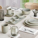 A modern dining table set with ash gray matte finish porcelain dishes, bowls, mugs, and glassware arranged neatly with silverware and white napkins.
