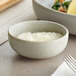 A small, round, ash gray bowl filled with finely grated white cheese, placed on a table next to a fork and napkin.