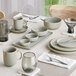 A modern dining table set with ash gray matte finish porcelain dishes, bowls, mugs, and glassware arranged neatly with silverware and white napkins.