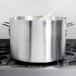 A large silver Vollrath sauce pot on a stove with a wooden spoon.