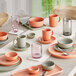 A table set with matte porcelain dinnerware in shades of terra cotta and gray, accompanied by glassware and cutlery.