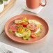 A terra cotta-colored plate with a fresh salad of sliced tomatoes, mozzarella, herbs, and a drizzle of olive oil.