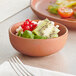 A small terra cotta-colored bowl containing sliced kiwi, red currants, green leaves, and white round toppings.