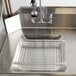 A stainless steel pre-rinse basket in a sink with holes.