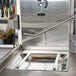 A stainless steel pre-rinse basket with a metal tray and holes in a commercial kitchen sink.