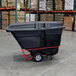 A black Rubbermaid hinged dome lid on a black tilt truck in a warehouse.