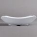 A close up of a Carlisle white square melamine bowl with a curved edge on a gray surface.