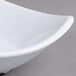 A close-up of a white Carlisle square melamine bowl with a curved edge.