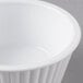 A close-up of a white Carlisle fluted plastic ramekin with a rim on a gray surface.