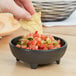 A person holds a chip over a bowl of salsa on a table and dips it.