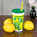 A 16 oz. plastic lemonade cup with a green lid and straw next to lemons.