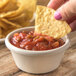 A person holding a chip dipping it into a bowl of salsa.