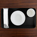 A black rectangular Cambro tray with a white plate and a cup on it.