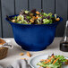 A Tablecraft cobalt blue cast aluminum tulip bowl filled with salad and bread on a table in a salad bar.