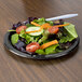A plate of salad with a fork on a black velvet paper plate.